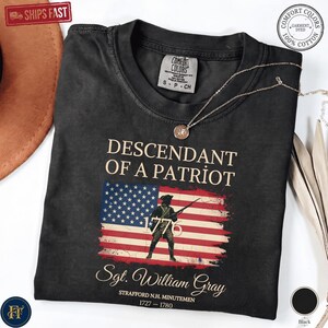 Pode incluir: Uma t-shirt preta de gola redonda com o texto "DESCENDANT OF A PATRIOT" sobre um gr&aacute;fico de um soldado segurando um rifle em frente a uma bandeira americana. Abaixo da bandeira, o texto diz "1776", "Sgt. William Gray" e "STRAFFORD N.H. MINUTEMEN 1727-1780".