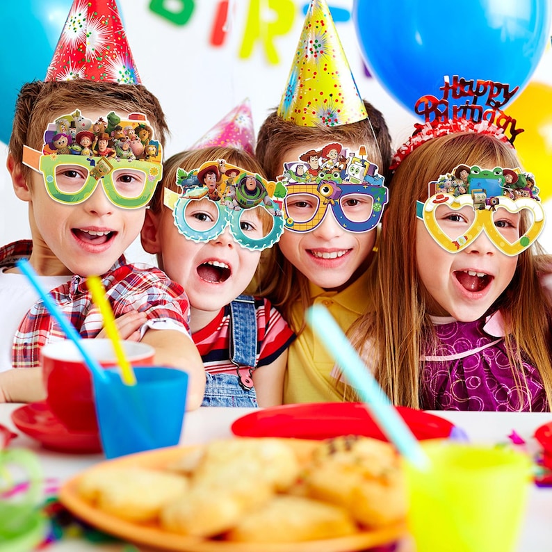May include: Four children wearing colourful party hats and paper glasses featuring Toy Story character graphics. The glasses have various frame shapes including round, square, and heart-shaped designs, all decorated with images of animated characters.