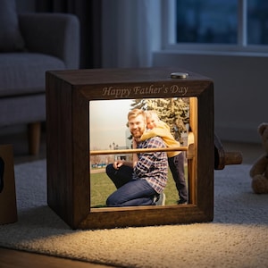 May include: A wooden photo cube with a picture of a man and child, illuminated from within. The cube has the words "Happy Father's Day" engraved on the top. The cube is sitting on a light-colored rug.