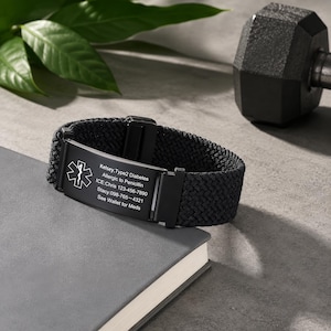 May include: A black medical alert bracelet featuring a woven nylon band and a rectangular metal plate. The plate displays the Star of Life symbol and engraved text: Kelsey, Type2 Diabetes, Allergic to Penicillin, ICE: Chris 123-456-7890, Stacy: 098-765-4321, See Wallet for Meds.