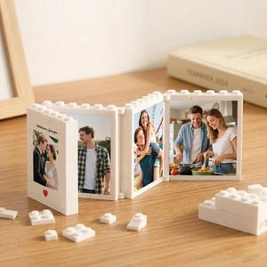 May include: A white plastic building block photo frame featuring four hinged panels displaying various photographs of couples. The first panel includes the text "Williams-Jennifer" and a small red heart icon. Several loose white building bricks are scattered.