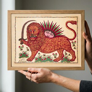 May include: A framed rectangular print featuring a stylized illustration of a lion holding a curved sword. The lion has a sun face on its back with green rays. The artwork includes small floral motifs, a decorative border, and Persian script.