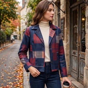 Può includere: Un blazer blu navy con un motivo patchwork a quadri rossi e beige, colletto a revers e due bottoni frontali. La giacca è indossata sopra un maglione a collo alto color crema con jeans blu scuro, tenendo in mano un bicchiere di caffè.