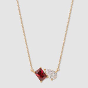 May include: A gold necklace with two gemstones: a rectangular, deep red stone and a pear-shaped, clear stone. The stones are set close together, suspended from a delicate chain. The necklace is a simple, elegant design.