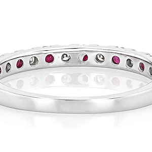 K&ouml;nnte beinhalten: Ein silberner Ring mit einem Band aus abwechselnd roten Edelsteinen und klaren Steinen. Der Ring ist vor einem wei&szlig;en Hintergrund platziert, was die Farbe der Edelsteine und die polierte Oberfl&auml;che des Rings hervorhebt.