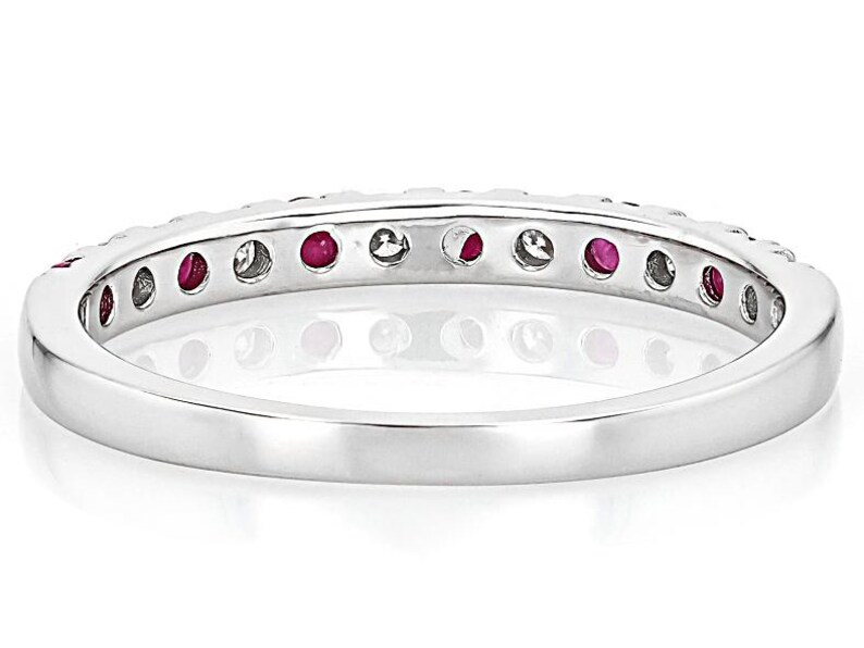 K&ouml;nnte beinhalten: Ein silberner Ring mit einem Band aus abwechselnd roten Edelsteinen und klaren Steinen. Der Ring ist vor einem wei&szlig;en Hintergrund platziert, was die Farbe der Edelsteine und die polierte Oberfl&auml;che des Rings hervorhebt.