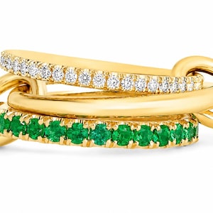 Puede incluir: Tres anillos de oro entrelazados. Uno está incrustado con pequeños diamantes blancos, otro es de oro liso y el tercero está forrado con pequeñas esmeraldas verdes. Los anillos están unidos en un diseño único.