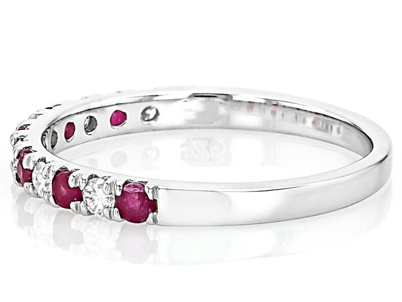 K&ouml;nnte beinhalten: Ein silberner Ring mit abwechselnd roten Rubinen und klaren Diamanten. Die Edelsteine sind eng am Band angeordnet. Der Ring hat eine polierte, reflektierende Oberfl&auml;che. Der Ring wird vor einem wei&szlig;en Hintergrund gezeigt.