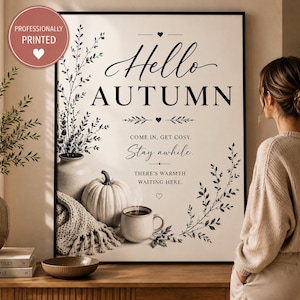 May include: A rectangular wall art print featuring the text Hello AUTUMN, COME IN, GET COSY, Stay awhile, THERE'S WARMTH WAITING HERE. The design includes a white pumpkin, a steaming mug, a textured throw blanket, and botanical illustrations.