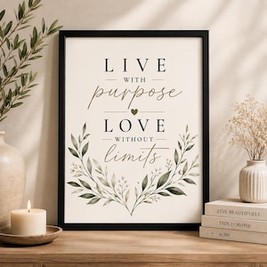 May include: A framed wall art print featuring the text LIVE WITH purpose LOVE WITHOUT limits in a mix of serif and script fonts. The design includes a small heart icon and a decorative illustration of green leafy branches at the bottom.