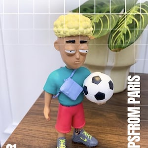 Könnte beinhalten: Eine stilisierte Figur mit blondem Lockenhaar, bekleidet mit einem türkisfarbenen T-Shirt, einer hellvioletten Umhängetasche und pinkfarbenen Shorts. Die Figur hält einen schwarz-weißen Fußball und trägt graue Sneaker mit neongelben Schnürsenkeln. Text 01 JUNE CLIPSFROM PARIS.