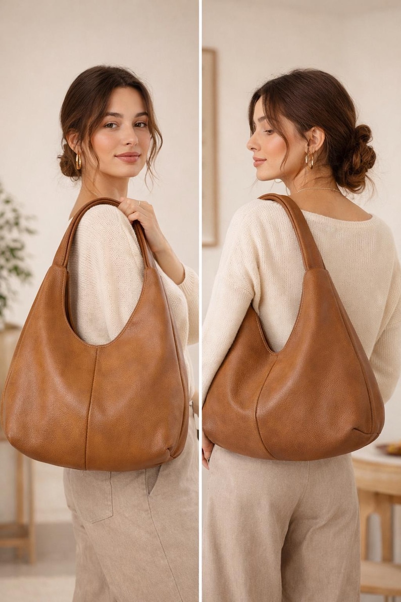 May include: A large, brown leather shoulder bag with a curved design. The bag has a single strap and is held by a person. The bag is a warm, medium brown colour and appears to be made of soft leather. The bag is a stylish accessory.