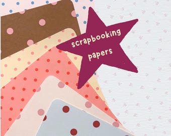 May include: A collection of stacked scrapbooking papers featuring various polka dot patterns in shades of light blue, brown, cream, coral, and grey. A dark purple star-shaped cutout is placed on top with the text scrapbooking papers printed in white.