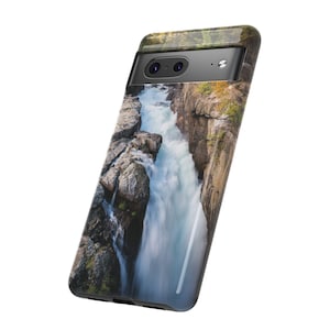 May include: A smartphone case featuring a high-resolution photographic print of a rushing waterfall cascading through a narrow, rocky canyon. The case has a black camera bar cutout at the top, revealing two circular lenses and a flash.