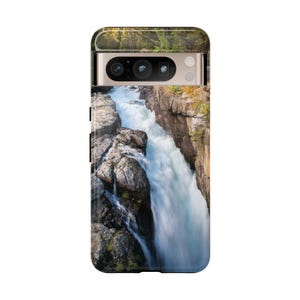 May include: A rectangular smartphone case featuring a high-resolution photographic print of a rushing river flowing through a narrow, rocky canyon. The case includes a horizontal camera cutout at the top, revealing the phone's triple-lens camera system.