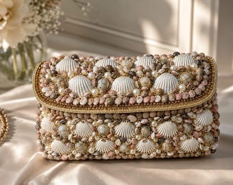 May include: A rectangular clutch bag completely covered in a dense arrangement of white scallop shells, small round pearls, and various tan, pink, and grey textured stones. The edges are finished with a thin gold metallic trim.