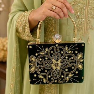 Pode incluir: Uma bolsa clutch retangular de veludo verde-escuro com missangas douradas intrincadas e bordados num padrão floral. A bolsa tem uma pega de metal dourado e um fecho transparente em forma de cristal facetado na borda superior.