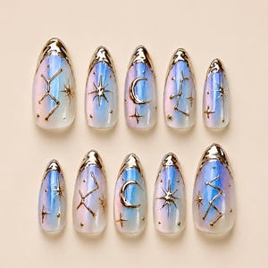 May include: Set of ten iridescent false nails with a gold metallic trim. Each nail features a celestial design with stars, moons, and constellations in gold. The nails have a rounded almond shape.
