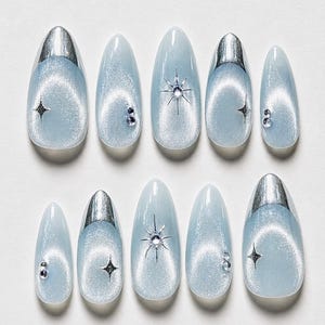 May include: A set of ten light blue press-on nails with a silver metallic tip. Each nail features a shimmering effect, with star and gem embellishments. The nails are oval-shaped, offering a stylish and elegant aesthetic.