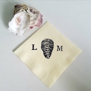 May include: A cream-colored square napkin with a black oyster illustration and the letters "L" and "M" printed on it. An open oyster shell with purple and white hues is in the upper left corner.
