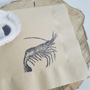 Pode incluir: Guardanapo de papel bege com uma ilustra&ccedil;&atilde;o de lagosta preta. O guardanapo tem uma borda canelada e &eacute; colocado em uma fatia de madeira. Uma concha de ostra branca est&aacute; no canto superior esquerdo.