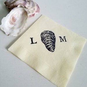 May include: A cream-colored paper napkin with a black oyster illustration and the letters "L" and "M". An open oyster shell with purple and white hues is in the background. The napkin has a ribbed border.