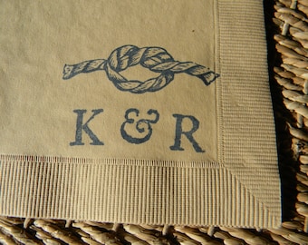 May include: Tan paper napkin with a navy blue nautical knot design and the initials "K & R". The napkin has a textured border and is likely for a wedding or nautical-themed event.