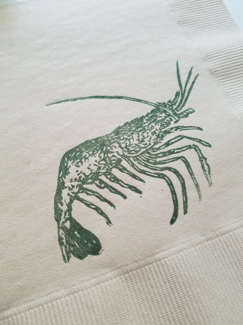 Pode incluir: Ilustra&ccedil;&atilde;o de um camar&atilde;o verde impressa em um guardanapo creme. O camar&atilde;o &eacute; detalhado com v&aacute;rias pernas, antenas e um corpo segmentado. O guardanapo tem uma borda texturizada e canelada.