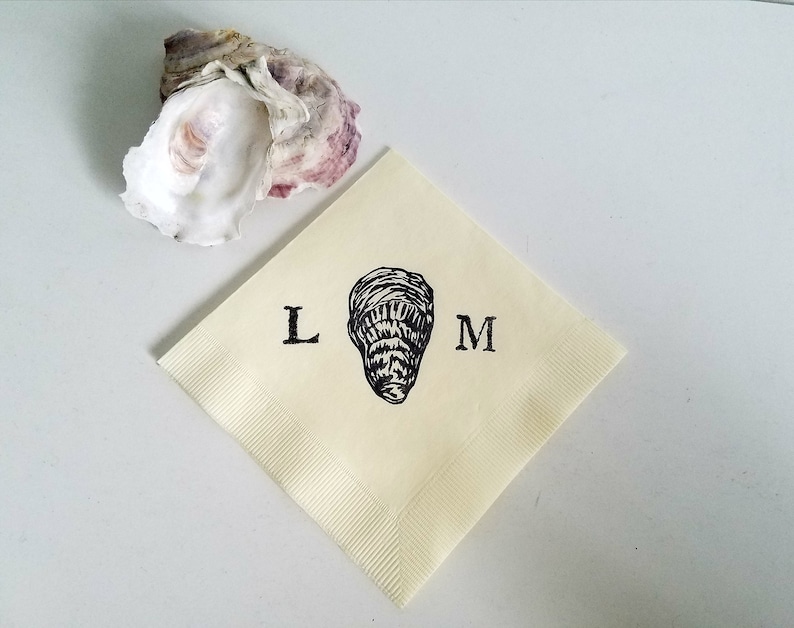 May include: A cream-colored square napkin with a black oyster illustration and the letters "L" and "M" printed on it. An open oyster shell with purple and white hues is in the upper left corner.