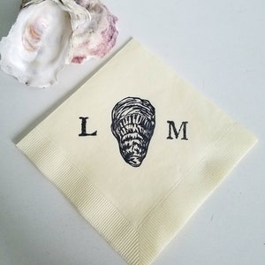 May include: A cream-colored square napkin with a black oyster illustration and the letters "L" and "M". An open oyster shell with purple and white hues is in the background. The napkin has a ribbed border.