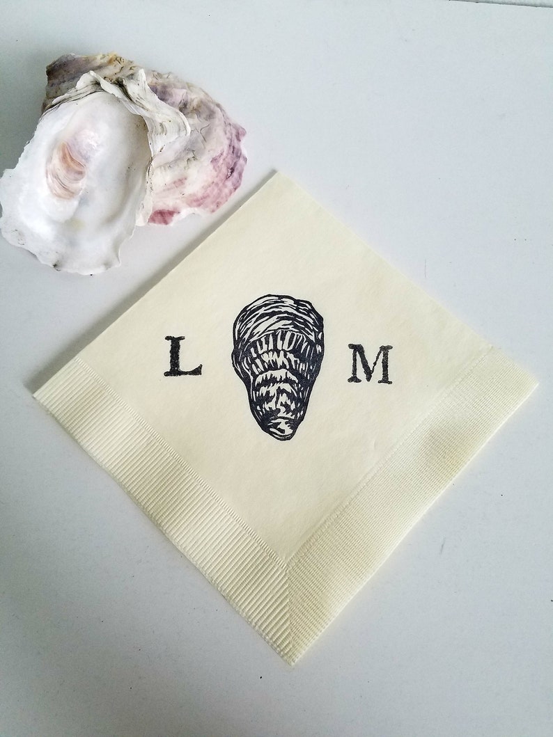 May include: A cream-colored square napkin with a black oyster illustration and the letters "L" and "M". An open oyster shell with purple and white hues is in the background. The napkin has a ribbed border.