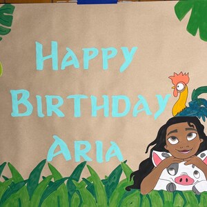 May include: A tan paper banner featuring the hand-painted light blue text HAPPY BIRTHDAY ARIA. The design includes a cartoon character with long dark hair, a small pig, and a rooster, surrounded by green tropical leaves and grass illustrations.