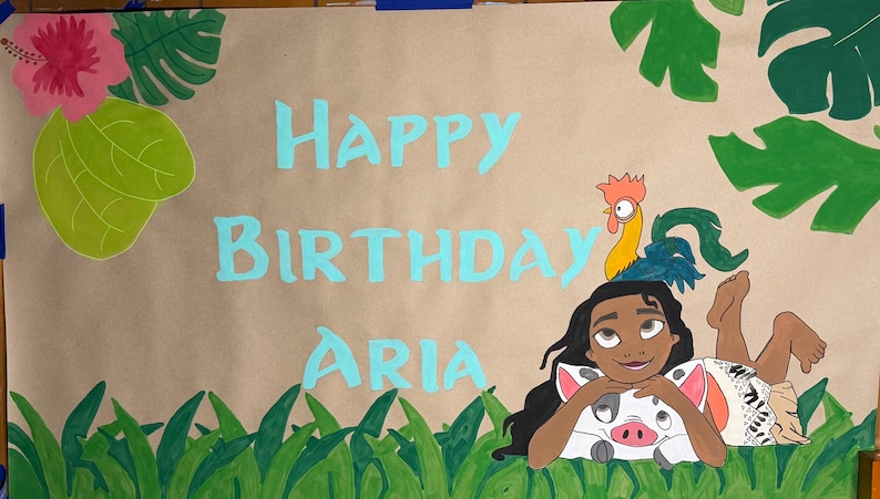 May include: A tan paper banner featuring the hand-painted light blue text HAPPY BIRTHDAY ARIA. The design includes a cartoon character with long dark hair, a small pig, and a rooster, surrounded by green tropical leaves and grass illustrations.
