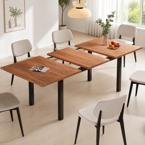 May include: An extendable dining table with a rectangular wooden top and black metal legs, surrounded by six chairs featuring light gray upholstered seats and black frames. The table is shown in an extended position with a central leaf visible.