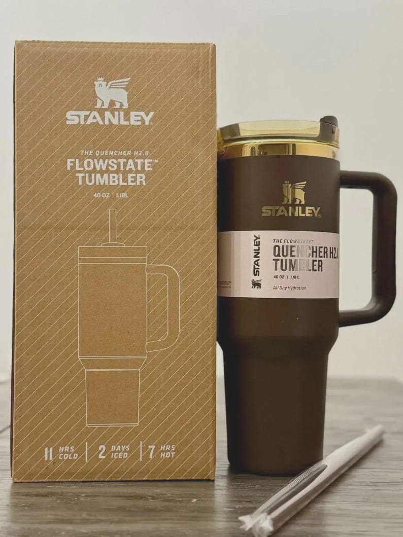 Puede incluir: Un vaso Stanley Flowstate marr&oacute;n con tapa y asa doradas, junto a su caja de cart&oacute;n. La caja y el vaso presentan el logotipo de Stanley y detalles del producto, incluyendo "40 oz | 1.18L". El vaso est&aacute; dise&ntilde;ado para la hidrataci&oacute;n durante todo el d&iacute;a.