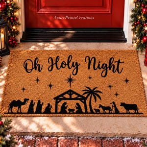 May include: A rectangular brown coir doormat featuring the black text Oh Holy Night. The design includes a black silhouette of a nativity scene with a stable, palm tree, camel, animals, and figures under a starry sky with a large star.