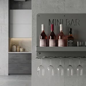 May include: A gray metal mini bar with the text "MINI BAR" cut out. It holds four bottles of wine and liquor, along with two small glasses. Six wine glasses hang below. The bar is mounted on a concrete wall.