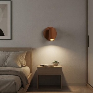 Può includere: Una lampada da parete cilindrica con finitura color terracotta opaco, dotata di una base circolare e di una testa direzionabile che emette una luce calda rivolta verso il basso, illuminando la parete sottostante.