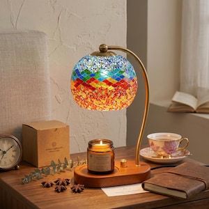 May include: A colorful mosaic glass lamp with a brass-colored curved arm. The lamp has a wooden base with a candle and a teacup on a saucer. A small clock and a box are also on the wooden surface.