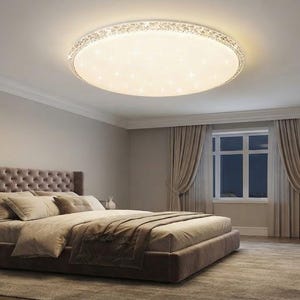 May include: A round, flush-mount ceiling light fitting with a white, circular diffuser and a decorative, textured silver-toned border. The light emits a warm, bright glow, illuminating the room with a star-like pattern across the surface.
