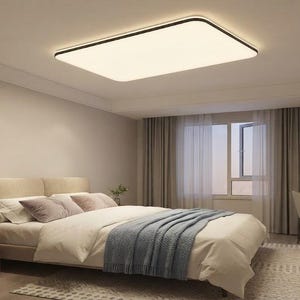 May include: A rectangular ceiling light fixture with a thin black frame and a white diffuser panel, emitting a soft, warm glow. The light is mounted flush against a white ceiling in a bedroom setting, providing even illumination across the room.