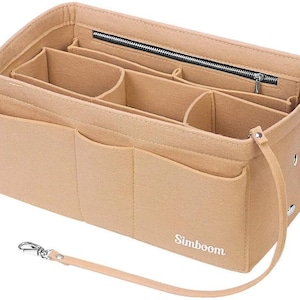 Op de afbeelding: Beige vilten handtas organizer met meerdere compartimenten en een ritssluiting aan de bovenkant. Voorzien van een afneembare riem en een zilverkleurige sluiting. De merknaam "Simboom" is gedrukt.
