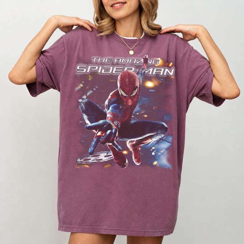 May include: A maroon t-shirt featuring a graphic of Spider-Man in a dynamic pose. The text "THE AMAZING SPIDER-MAN" is printed above the character. The shirt has short sleeves and a relaxed fit.