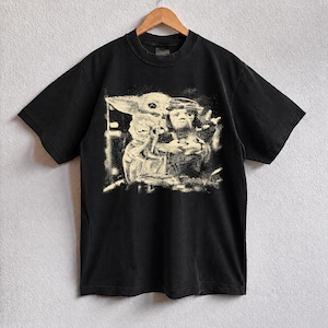 May include: Black t-shirt with a faded graphic of characters from a science fiction franchise. The design is in a light beige colour, giving it a vintage appearance. The t-shirt has short sleeves and a crew neck.