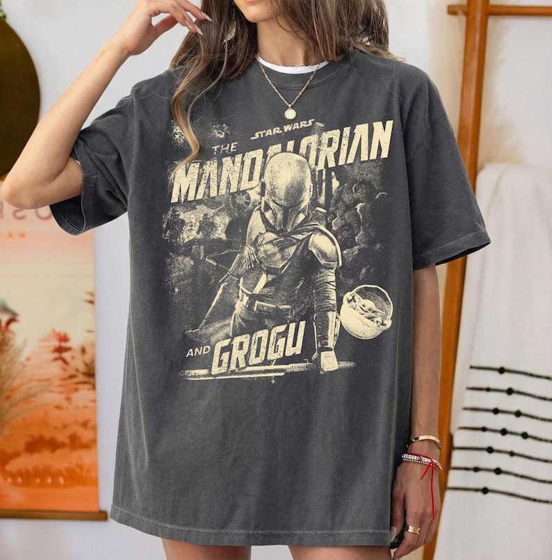 Pu&ograve; includere: T-shirt grigio scuro con grafica vintage di The Mandalorian e Grogu di Star Wars. Il design include il testo "The Mandalorian" e "Grogu" in stile vintage. La maglietta ha maniche corte e una vestibilit&agrave; ampia.