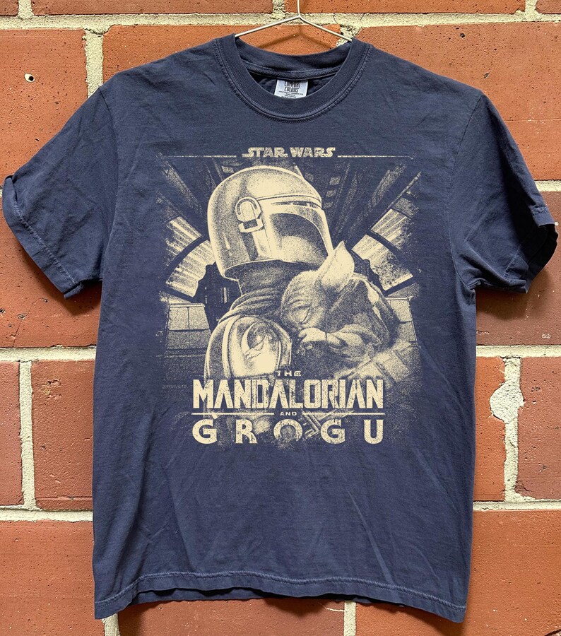 Puede incluir: Camiseta azul marino con un gr&aacute;fico de The Mandalorian y Grogu de Star Wars. El dise&ntilde;o incluye el texto "STAR WARS" encima de la imagen y "THE MANDALORIAN and GROGU" debajo.