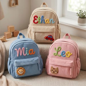 May include: Three corduroy backpacks in beige, blue, and pink. The beige bag features the name Ethan and a red car patch. The blue bag displays the name Mia and a lion patch. The pink bag shows the name Leo and a cat patch. Each has a front pocket.