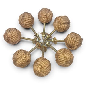 May include: A set of eight decorative rope knot knobs with brass-colored hardware. The knobs are made of tightly wound natural-colored rope, each attached to a bolt with a washer and nut. The knobs are arranged in a circular pattern.