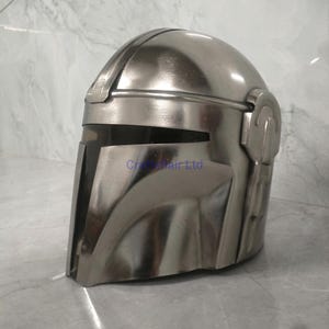 Pu&ograve; includere: Un casco Mandaloriano color argento, una replica del franchise di Star Wars. Il casco presenta una visiera a forma di T e una parte superiore arrotondata. La superficie riflette la luce, conferendogli un aspetto metallico.
