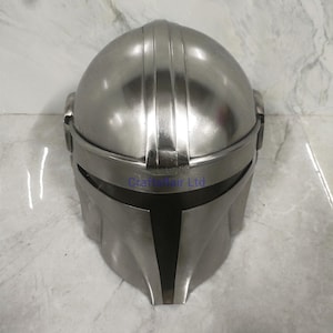 Pu&ograve; includere: Un casco color argento con una visiera a forma di T. Il casco ha una parte superiore arrotondata e una finitura metallica liscia. Il design include creste verticali e una prominente linea delle sopracciglia.